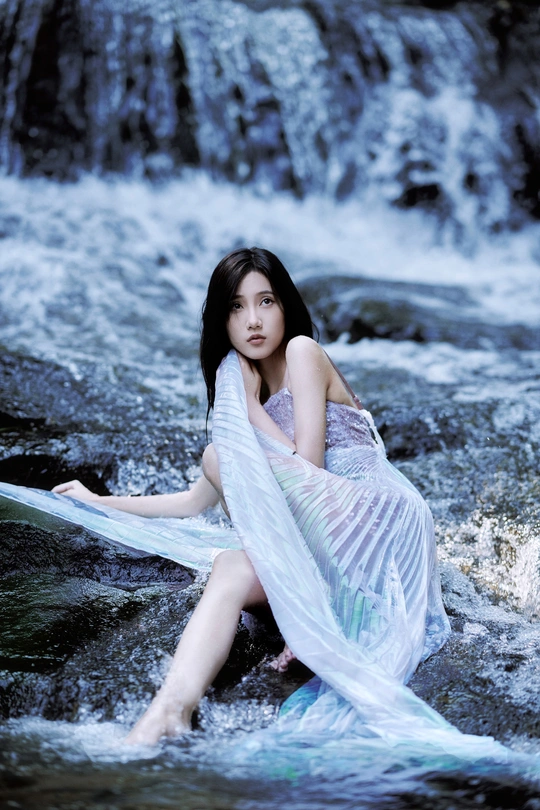 一个穿着蓝色连衣裙的美丽年轻女子坐在河边或小溪里的岩石上