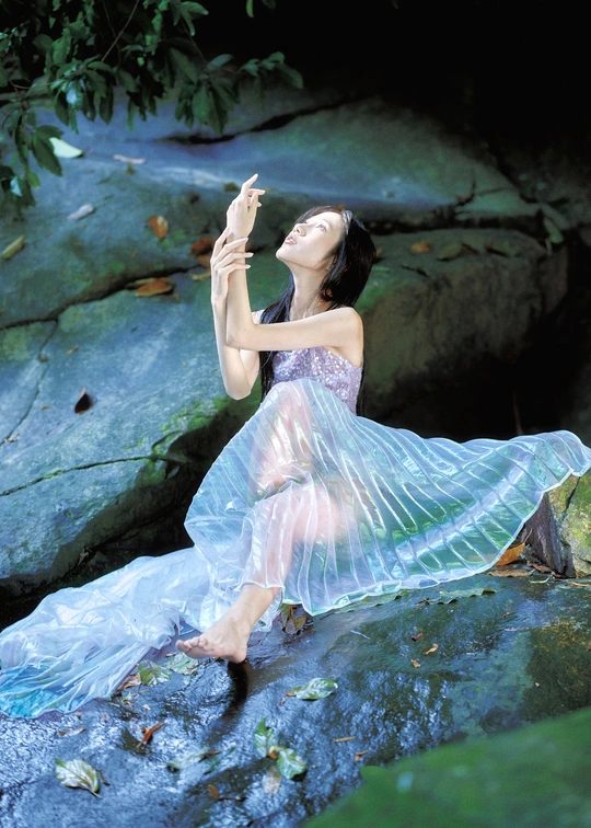 一个穿着蓝色连衣裙的美丽年轻女子坐在溪流中的岩石上