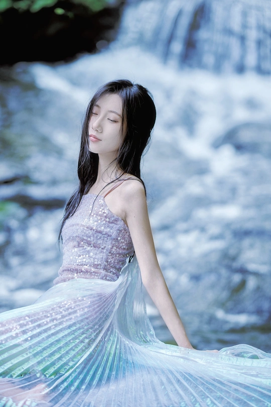 瀑布或小溪边穿着蓝色连衣裙的美丽年轻女子