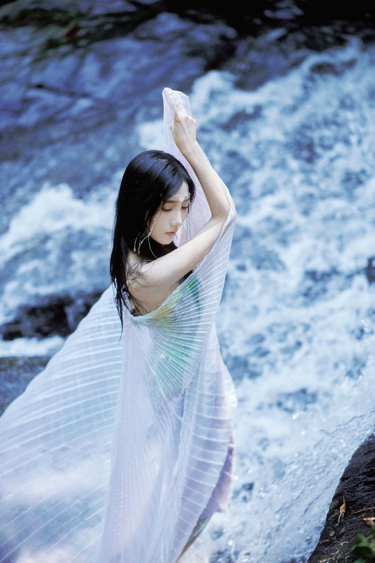 一位身穿白色连衣裙的年轻美女在碧水瀑布前摆姿势