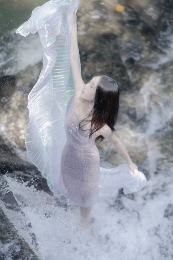 一个穿着漂亮连衣裙的年轻女子站在瀑布水中