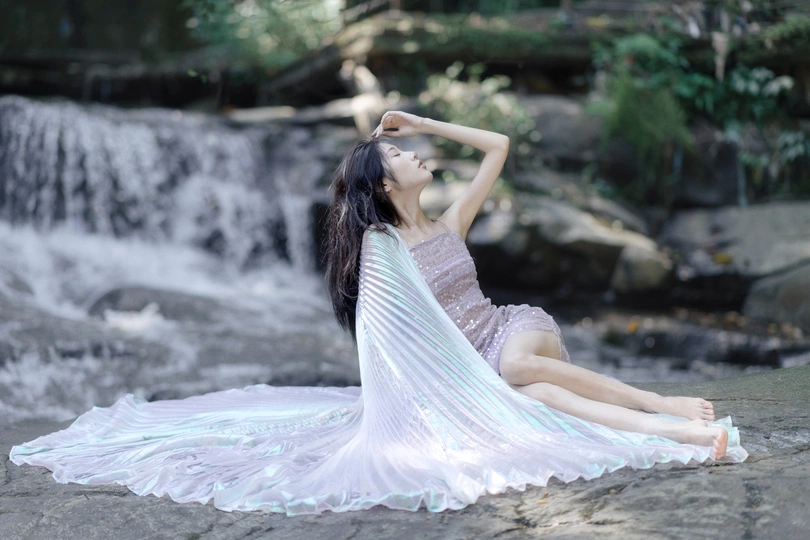 一个穿着白色连衣裙的年轻女子坐在瀑布前的岩石上