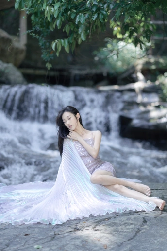 一个穿着漂亮蓝色连衣裙的年轻女子坐在瀑布前的岩石上