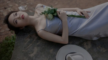 一位穿着白色连衣裙的美丽年轻女士戴着帽子和鲜花躺在岩石上