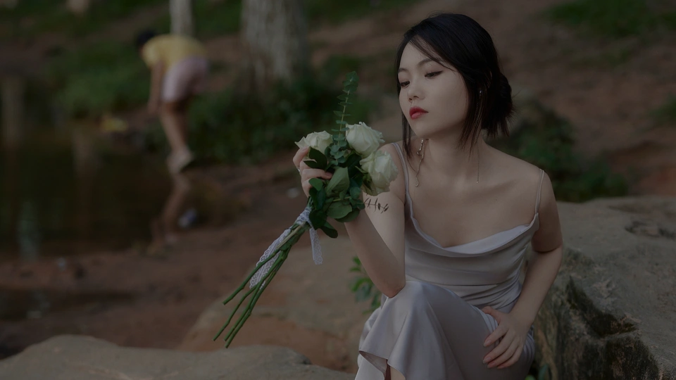 一位身穿白色连衣裙的年轻女子手持一束鲜花沿着岩石行走