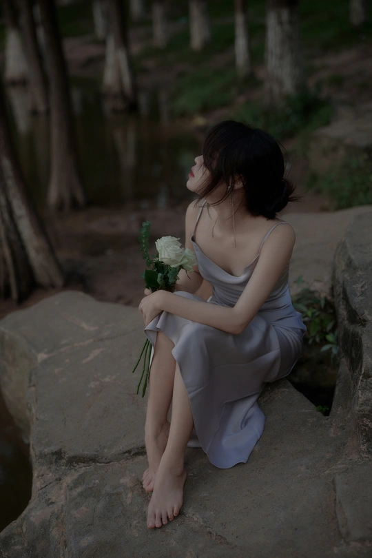 一位身穿蓝色连衣裙的年轻女子坐在岩石上 手里拿着一束白花