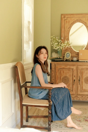一个年轻女子坐在一个木椅上 房间里有一面镜子。