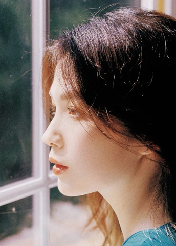 一位留着蓝色头发的年轻女子正在看窗户外。