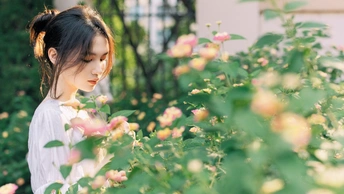 一个美丽的年轻女子站在一个花园里 手里拿着粉红色的玫瑰花。