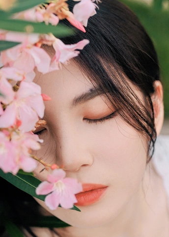 一位身着白色衣服 头戴粉色花朵 脸上还拿着花的年轻女子肖像。