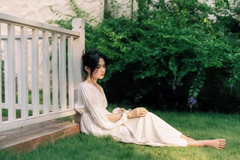 一个穿着白色连衣裙的年轻女子坐在院子里的一张长凳上