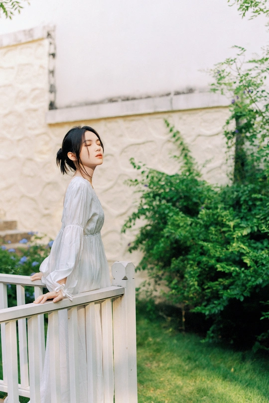 一个穿着白色连衣裙的年轻女子站在一堵白色栅栏旁边