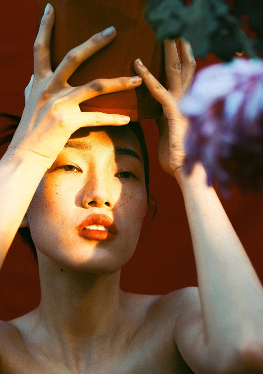 一个年轻女子双手捂住眼睛 头戴帽子 脸上有一朵花。