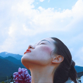 一位年轻女子举着一朵粉红色花向天空