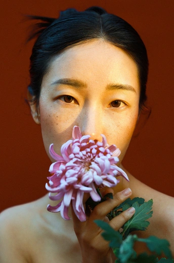 一位年轻女子手持粉色花朵靠近她的脸