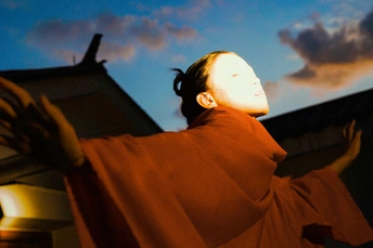 一个穿着长袍的年轻女子站在寺庙外面 太阳照亮了天空。