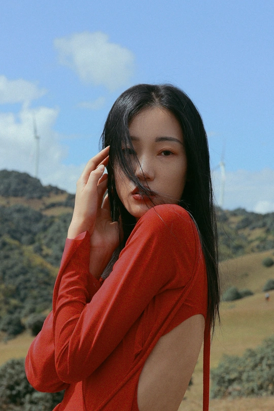 一位穿着红衬衫的年轻女子站在田野中 正在打电话。