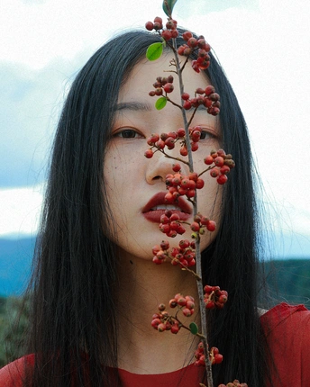 一位年轻女子用覆有红浆果的树枝遮住脸