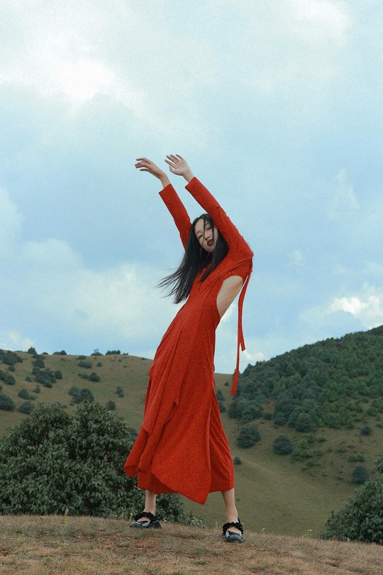 一位穿着长红裙子的女人站在田野中 伸开双臂。