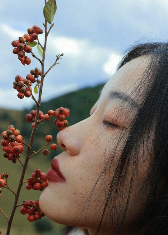 一位年轻女子闭着眼睛 手里拿着一个带红果实的树枝