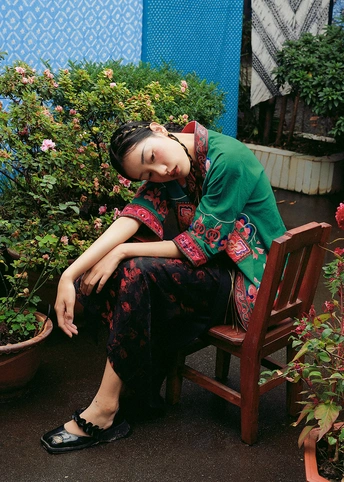 一个穿着连衣裙的年轻女子坐在木凳上 旁边是花和植物的盆栽。