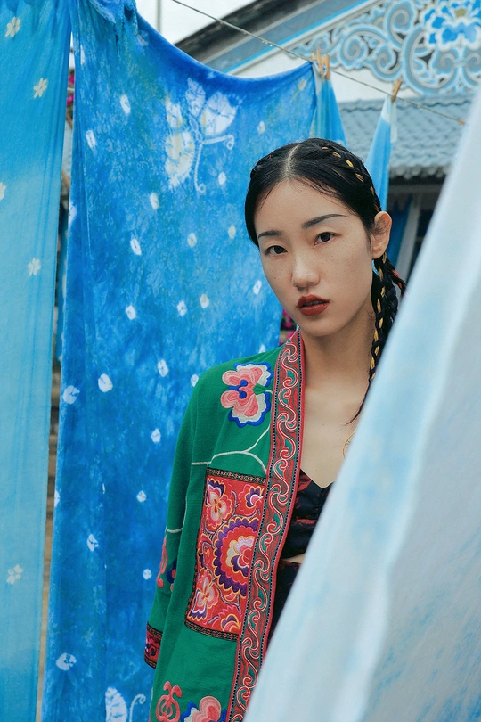 一位穿着传统服装的年轻女子站在一把蓝色雨伞下