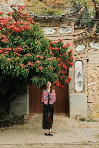 站在一栋建筑前 有一棵开红花的树