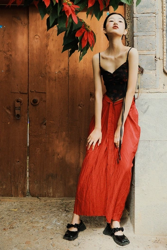 一位穿着黑色和红色连衣裙的年轻女子站在木质墙壁和门前