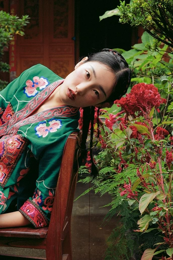 一位穿着绿色连衣裙的年轻女子坐在花园里的木凳上 周围是鲜花。