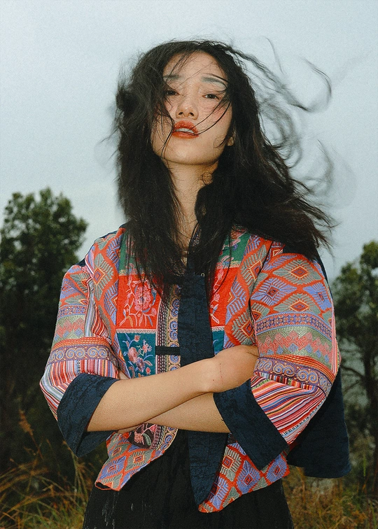 一位穿着彩色衬衫 长发飘飘 站在田野中的年轻女子