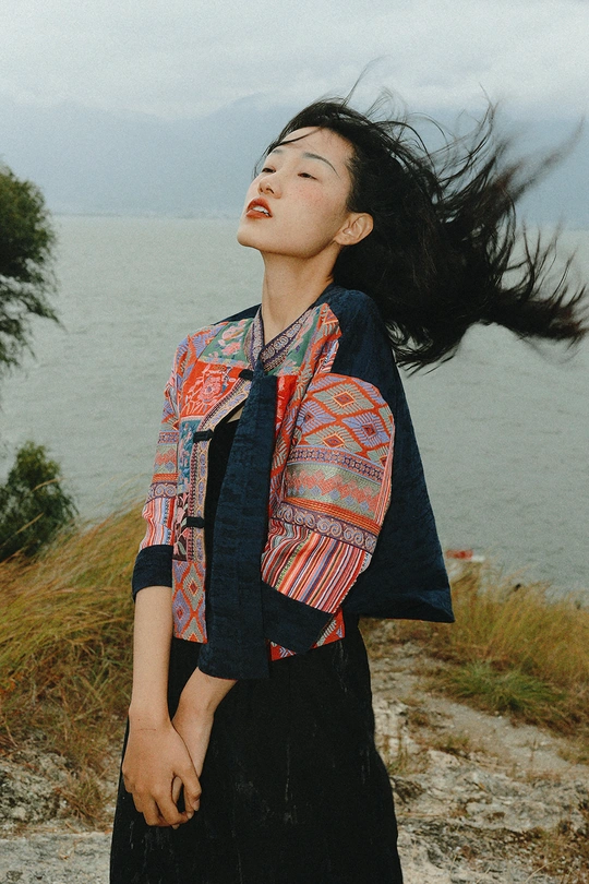 一位年轻女子穿着裙子在水面边的岩石上摆姿势 她的长发在风中飘动。