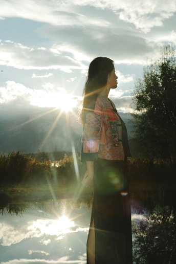 夕阳西下 一位女士站在湖边 阳光照耀在天空中 水面上波光粼粼。