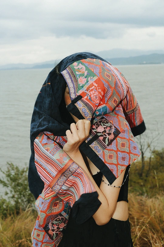 一个年轻女孩穿着一件披肩紧紧抱住自己的脸 站在一个俯瞰湖泊的悬崖上。