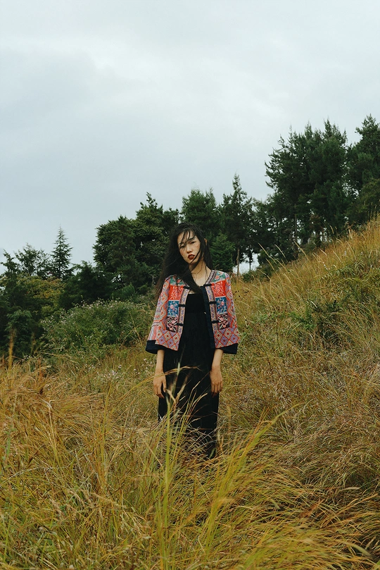 一位穿着长裙的年轻女子站在一片高草丛中