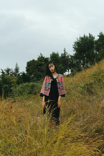 一位穿着长裙的年轻女子站在一片高草丛中