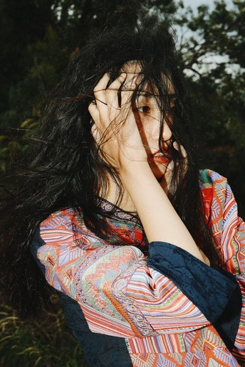 一个穿着花衬衫的年轻女子正在用手捂住脸打电话