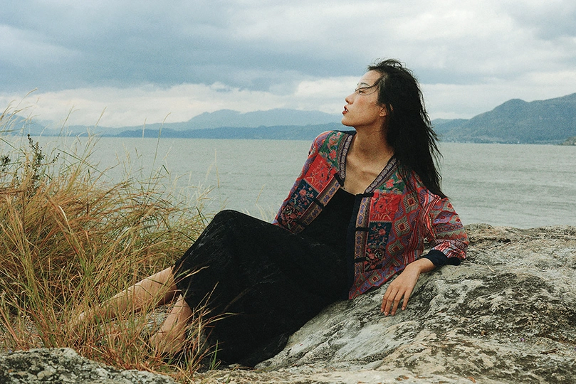 一位年轻女子坐在水体岩石岸边的一块岩石上