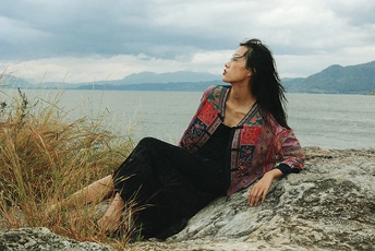 一位年轻女子坐在水体岩石岸边的一块岩石上