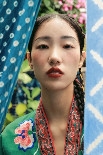 一位穿着传统服装的年轻女子在蓝色雨伞下摆姿势 唇色鲜红。