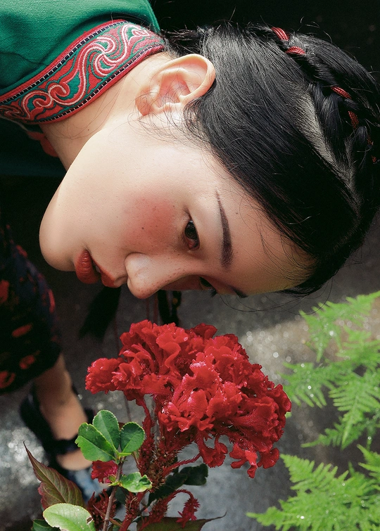 一个小女孩在花瓶里闻一朵红色的花 一个年轻女子在一旁看着。