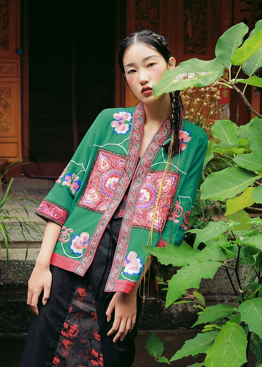 一位穿着中国传统服装的年轻女子在绿色植物前摆姿势