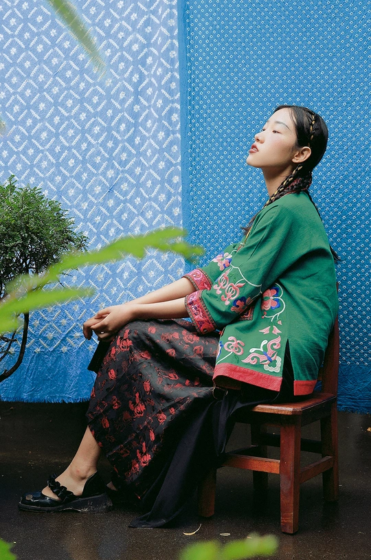 一个穿着绿色连衣裙的年轻女子坐在木椅上 带着一把蓝色雨伞。