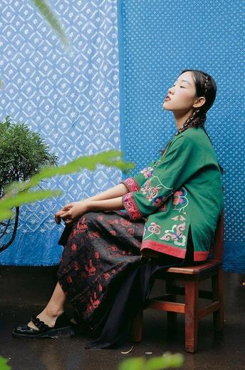 一个穿着绿色连衣裙的年轻女子坐在木椅上 带着一把蓝色雨伞。