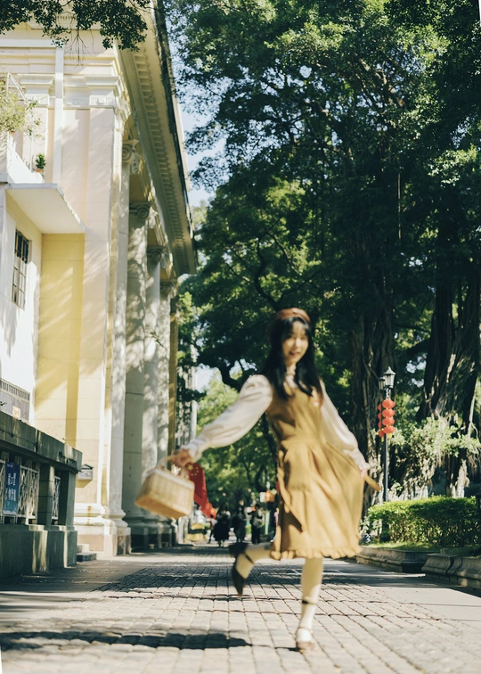 一位穿着黄色连衣裙的年轻女子 手提小篮子走在街上。