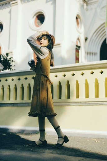 一位穿着外套 手持雨伞的年轻女子站在一个建筑物的 sidewalk 前 该建筑有一个小白色围墙。