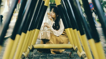 一个小女孩坐在街边的黄色杆子旁边。