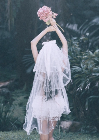 一位穿着白色连衣裙和面纱的女士拿着粉色花