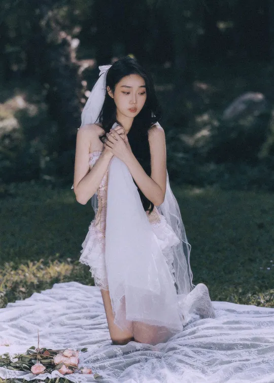 一个穿着白色婚纱的女人躺在草地上的一块毛毯上