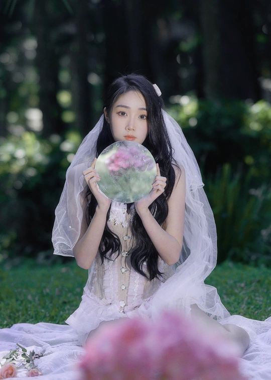 一位穿着白色长裙和面纱的年轻女子在草地上拿着花