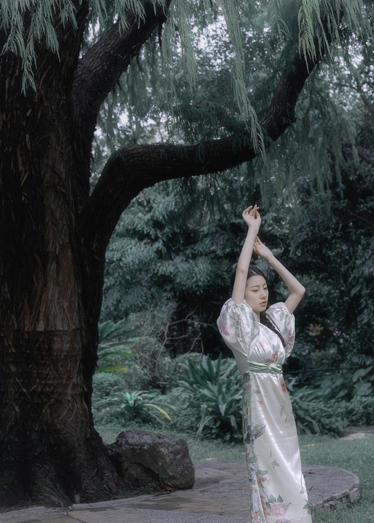 一位穿着传统裙子的年轻女子站在一棵树下